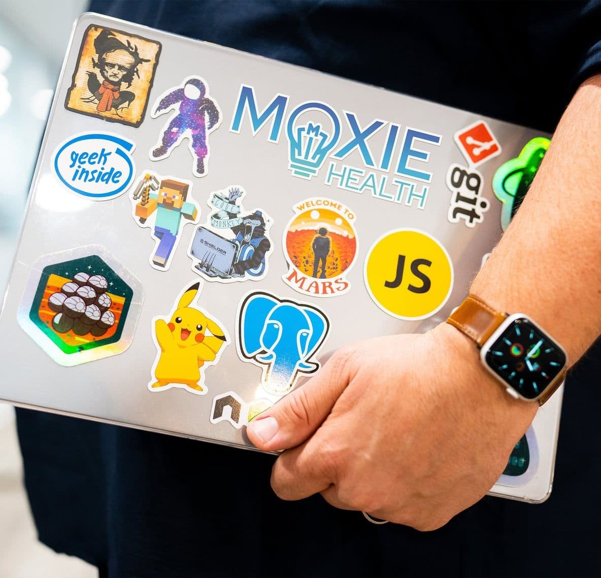 A Moxie Health team member carrying a laptop covered in stickers, including the Moxie Health logo